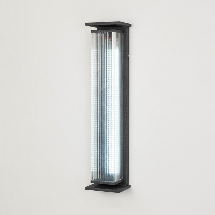 Black metal outdoor wall light on white background with ribbed glass shade for modern exterior decor.