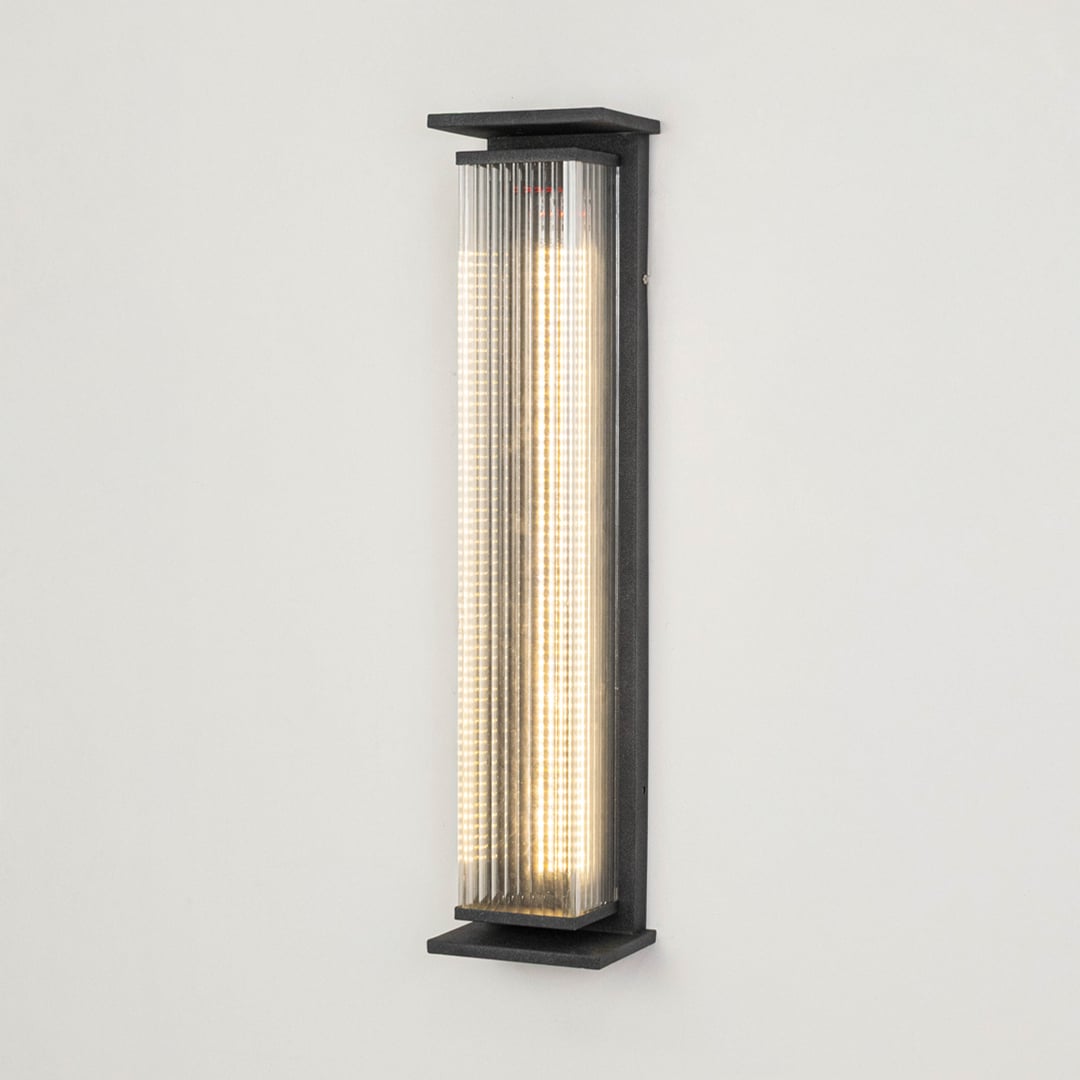 Modern outdoor wall light in black metal with ribbed diffuser displayed on white background highlighting sleek exterior lighting design.