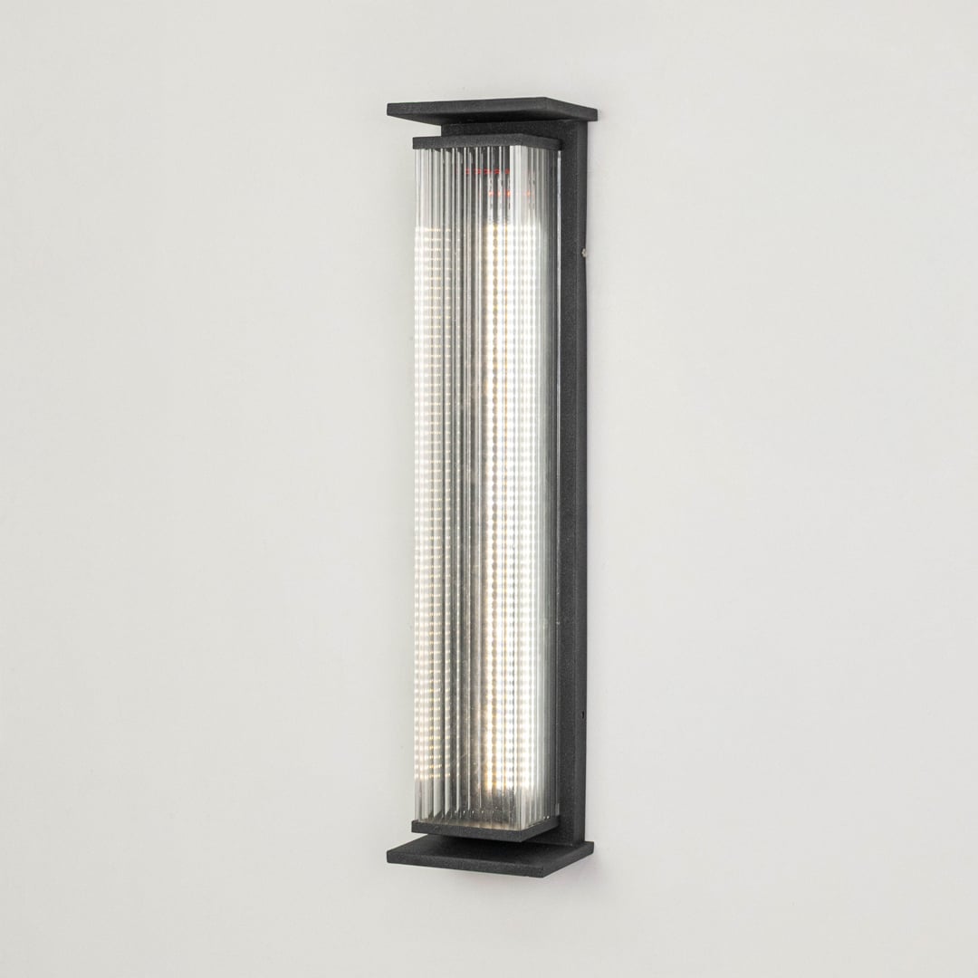 Modern outdoor wall light in black metal with ribbed diffuser displayed on white background highlighting sleek exterior lighting design.