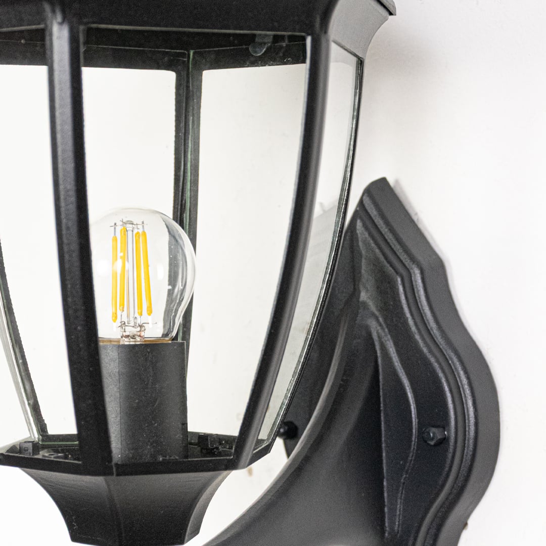 Closeup of outdoor wall light showing clear glass panel internal bulb visibility and sturdy black metal frame construction.
