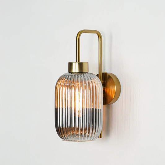 Gold metal wall light with ribbed glass shade emitting warm glow ideal for modern bedroom or hallway wall decor placement.