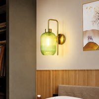 Modern green ribbed glass wall sconce light with brass arm on bedroom headboard wall for contemporary home decor styling.