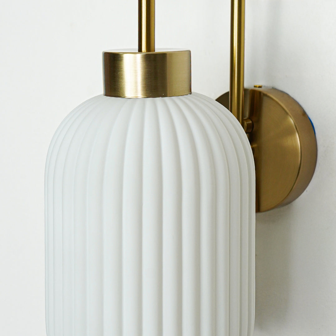 Closeup of gold metal wall light with white ribbed glass shade showcasing detailed texture and premium finish for modern decor styling.