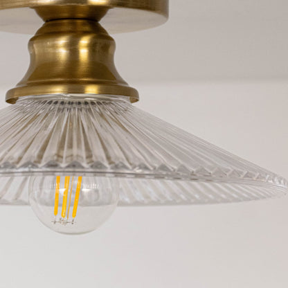 Closeup of ceiling light with brushed gold holder and transparent glass cone shade with exposed bulb for home lighting.