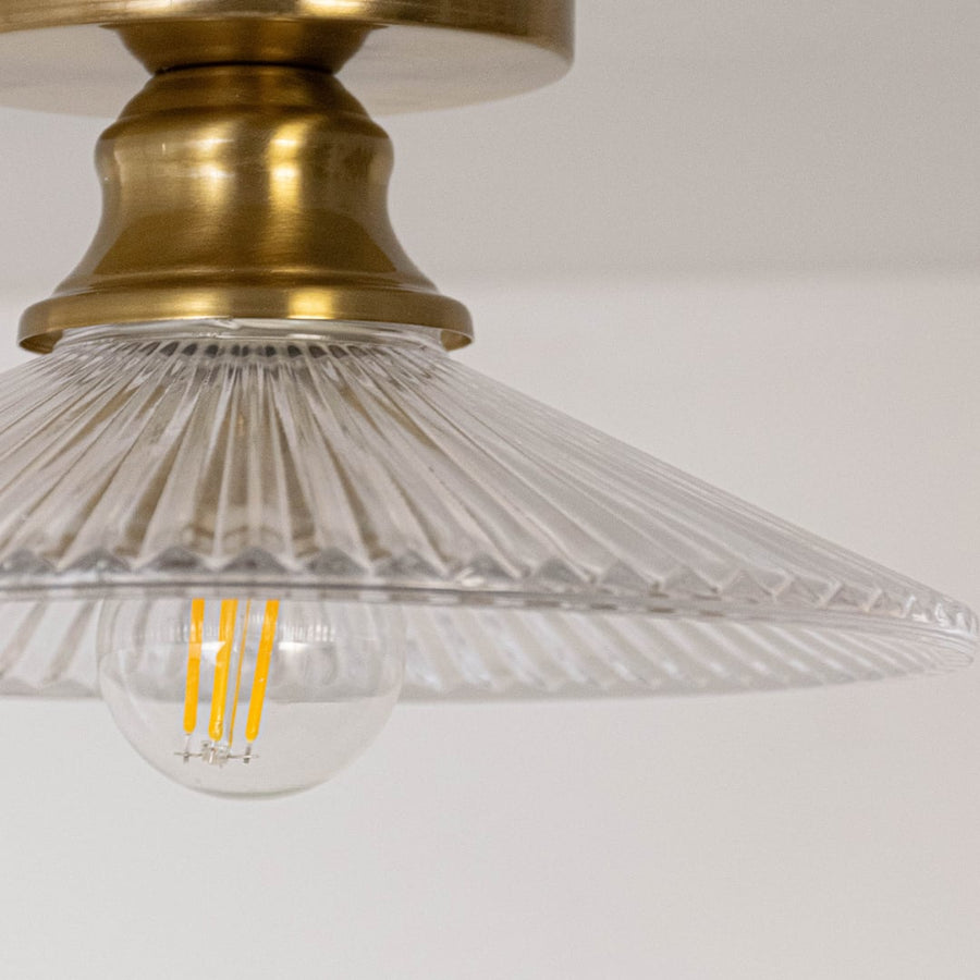 Closeup of ceiling light with brushed gold holder and transparent glass cone shade with exposed bulb for home lighting.