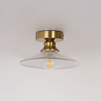Ceiling light with brushed gold base and transparent glass shade shown switched off with bulb on plain white background.