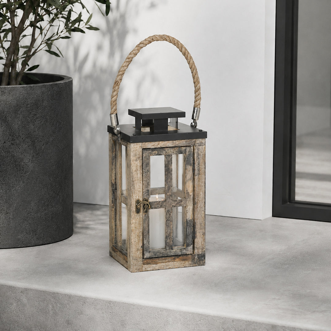 Wooden lantern with a rope handle on a concrete surface next to a potted plant.