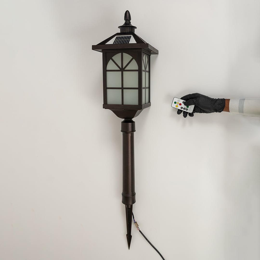 A bronze solar pathway lantern turned off on a white background highlighting the frosted glass panels metal window frame design and long pointed stake for outdoor placement.