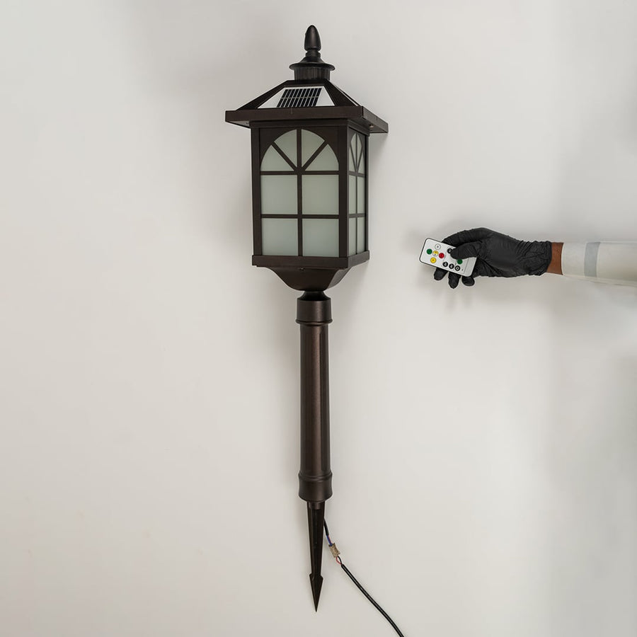 A bronze solar pathway lantern turned off on a white background highlighting the frosted glass panels metal window frame design and long pointed stake for outdoor placement.