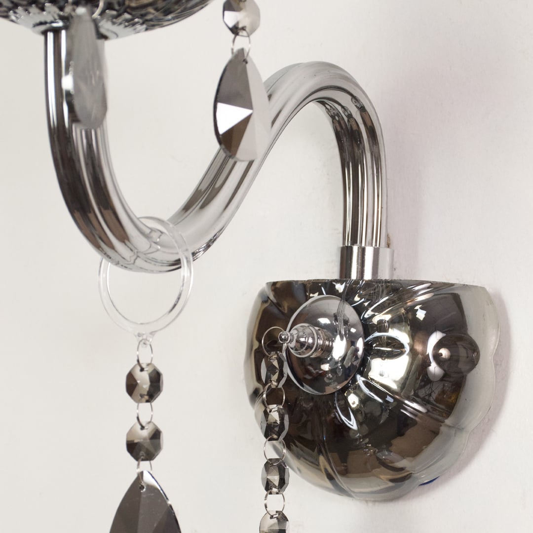 Closeup of chrome wall light showing curved metal arm and dark crystal drops for stylish modern interior lighting.