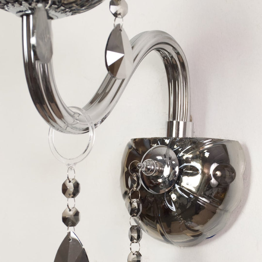 Closeup of chrome wall light showing curved metal arm and dark crystal drops for stylish modern interior lighting.