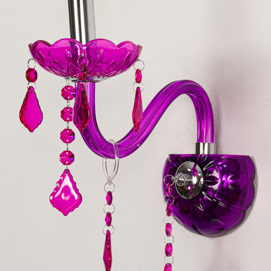 Closeup of pink wall light showing curved acrylic arm and bold crystal drops for eye catching modern interior lighting.
