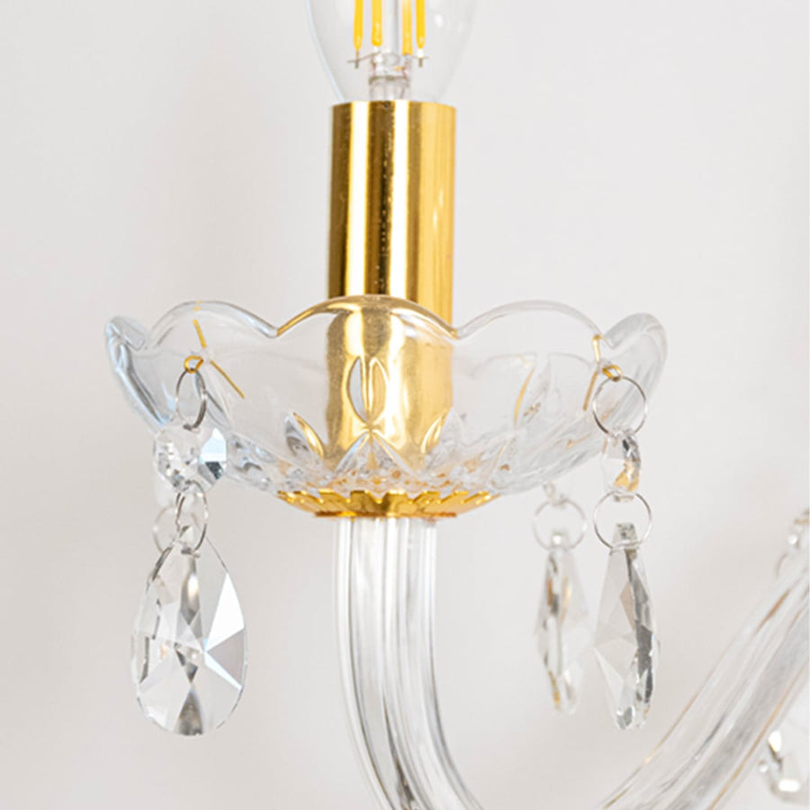 Closeup of crystal wall light showing clear glass arms hanging crystal drops and gold metal holder with luxury detailing.