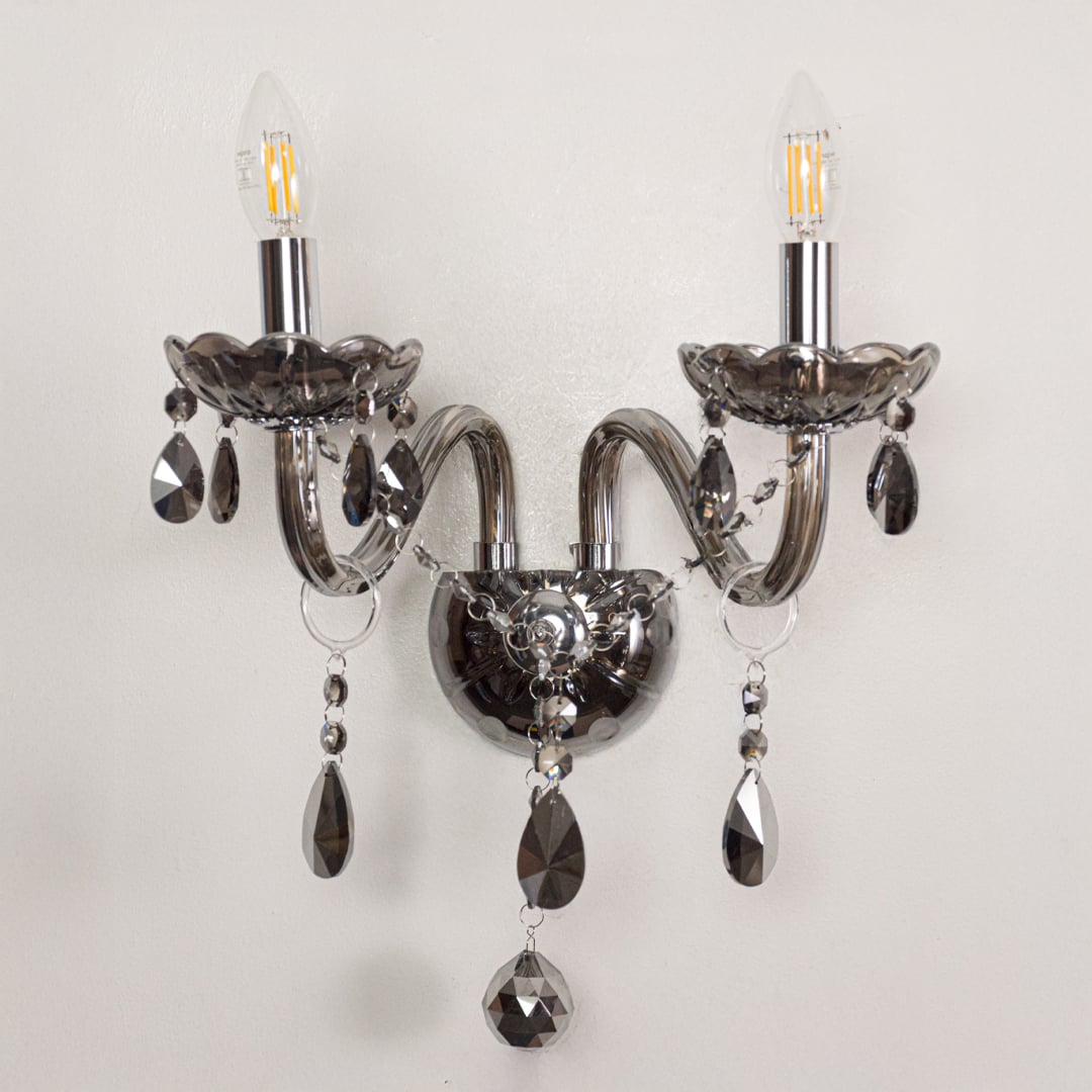 Closeup of chrome wall light showing curved metal arms and dark crystal drops for stylish modern interior lighting.