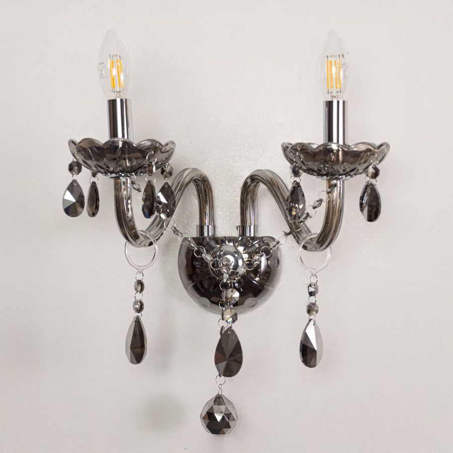 Closeup of chrome wall light showing curved metal arms and dark crystal drops for stylish modern interior lighting.