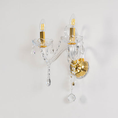 Crystal wall light with golden base dual candle design with crystal drops shown on off white background.