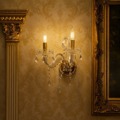 Gold metal wall sconce with crystal detailing and candle bulbs styled on patterned wall creating warm royal interior lighting.