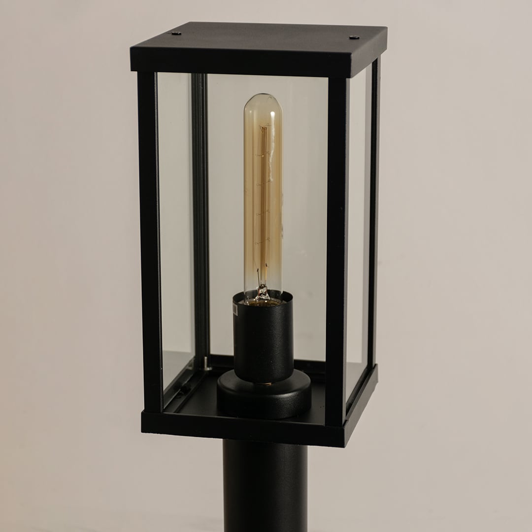 A closeup of a black outdoor bollard light showing detailed glass panels metal frame and bulb housing giving clear view of build quality and design details.