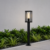 Modern black metal open cage cylindrical bollard post light fixture on garden path for contemporary yard landscape styling.