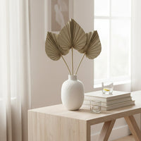 Three natural beige dried palm spear leaves arranged inside a white ceramic vase on a modern wooden entryway console table.