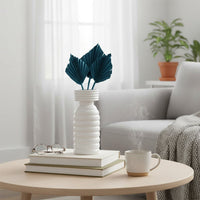 White ceramic vase with green leaves styled on coffee table near sofa adding fresh minimal accent to bright living room Decor.