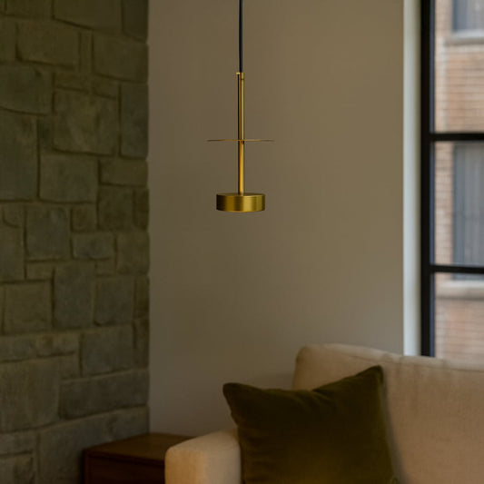 Halo brass pendant light turned on beside sofa and indoor plant adding warmth to minimalist home setting.