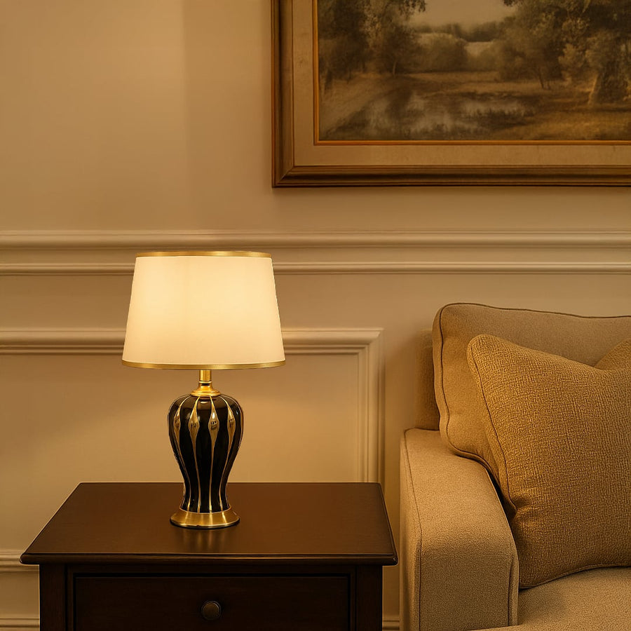 White shade dark ceramic table lamp on wooden side table with light on beside beige sofa for warm classic décor.