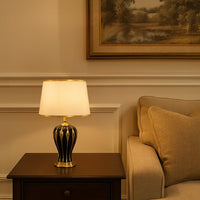 White shade dark ceramic table lamp on wooden side table with light on beside beige sofa for warm classic décor.