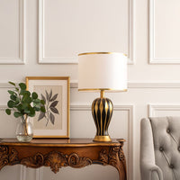 Elegant black gold table lamp styled on a wooden console with framed art and greenery.