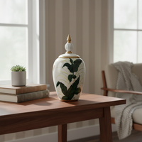 White ceramic decorative jar with green botanical artwork styled on a wooden table for elegant modern home decor settings.