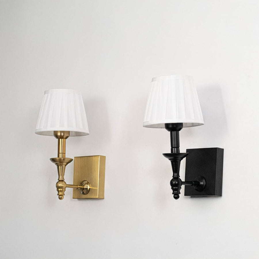 Black metal wall sconce with white pleated shade shown on a white background with lights off for clear detailing.