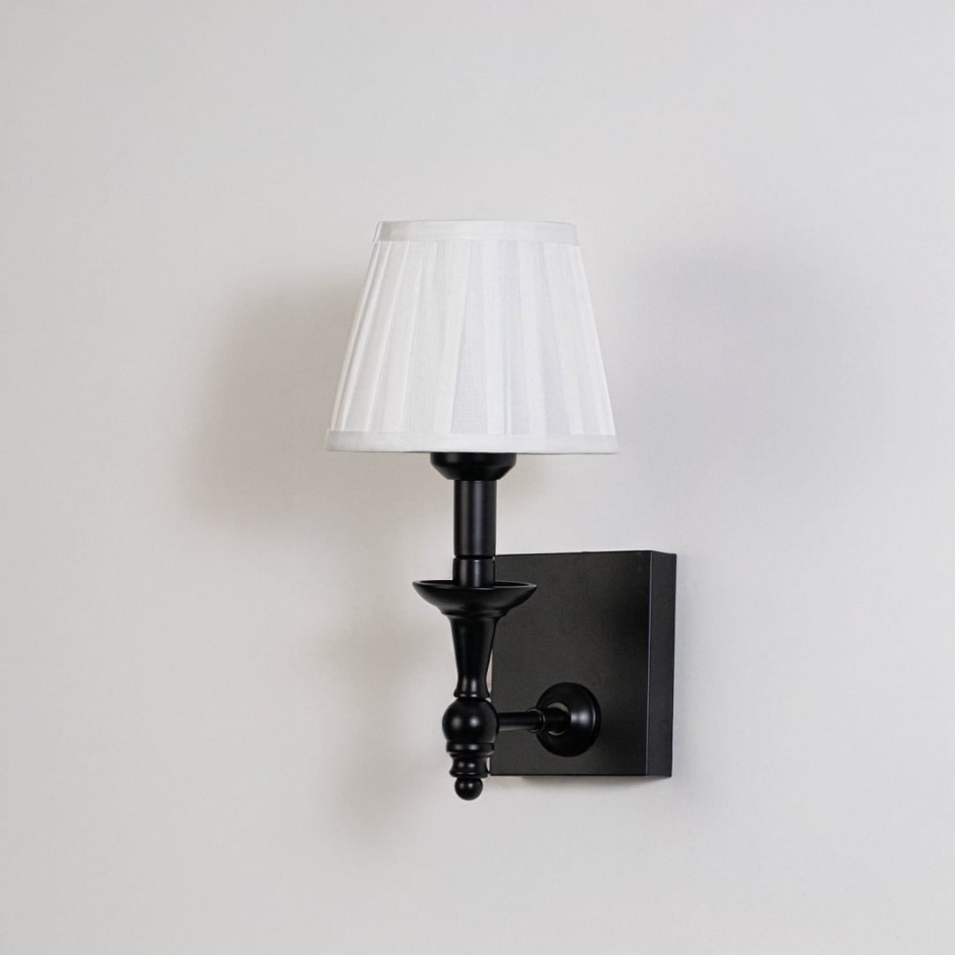 Black metal wall sconce with white pleated shade shown on a plain white background for accurate product clarity.
