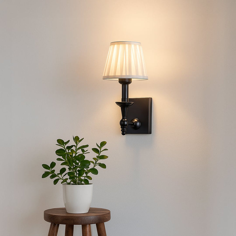 Black metal wall sconce with white pleated shade adding soft warm lighting to a modern elegant home interior.