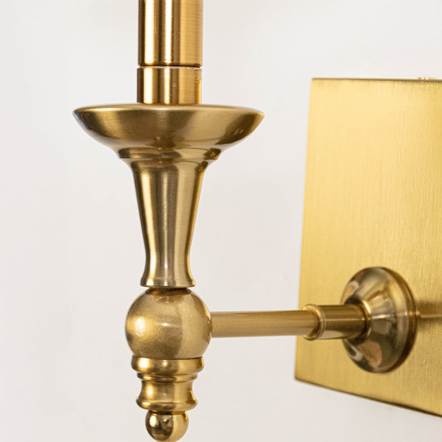 Closeup of gold wall sconce with white pleated lampshade highlighting classic elegant detailing and smooth finish.