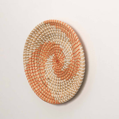 Side view of handcrafted natural cream seagrass wall basket with orange woven spiral wave pattern for boho wall decor.