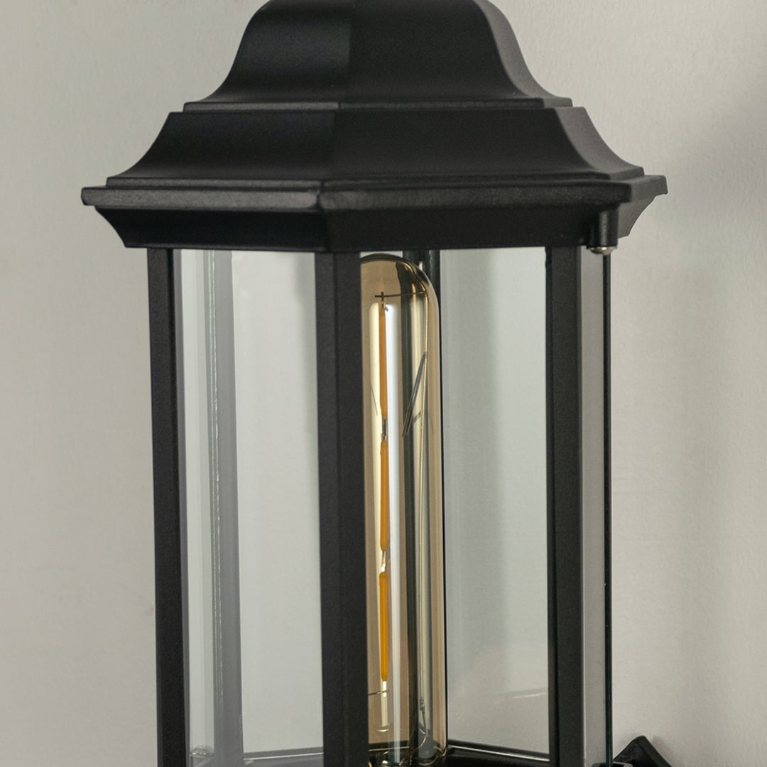 Closeup view of the black outdoor lantern showing detailed raindrop glass texture and elegant curved arm with warm light inside.