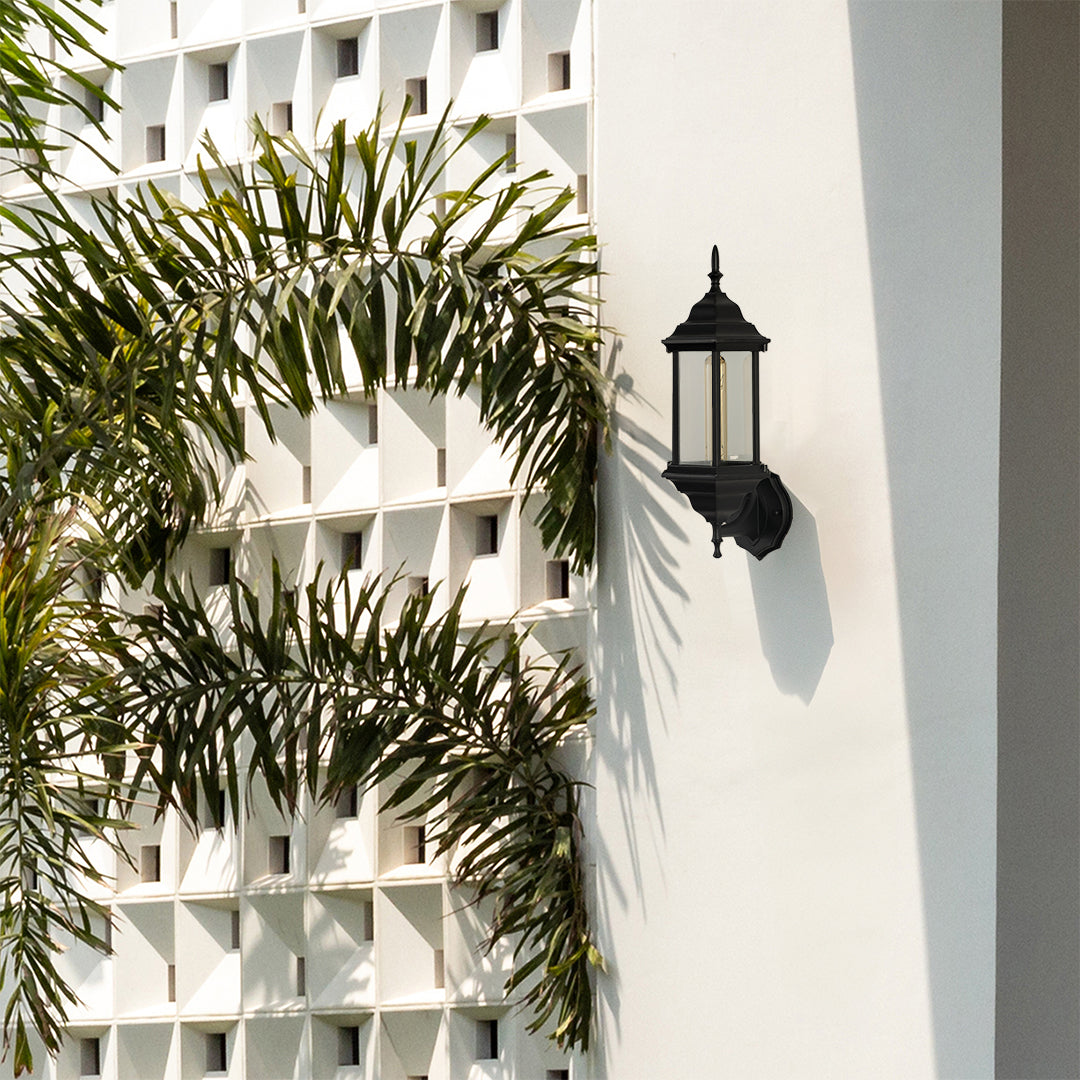 Stylish black outdoor lantern shown in a minimal setting featuring curved arm design and raindrop textured glass with warm lighting.