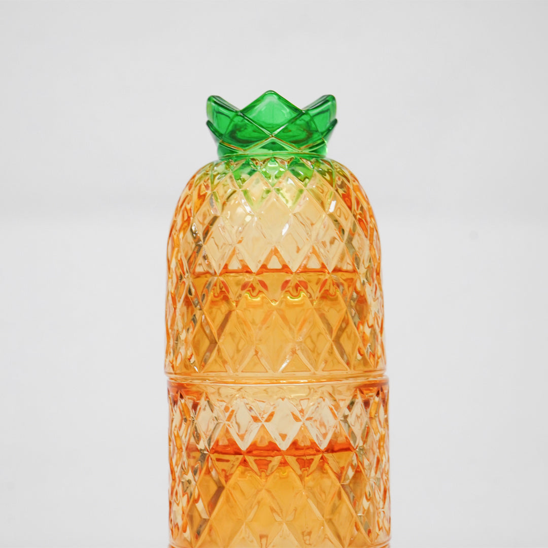 A translucent orange pineapple-shaped container with a textured diamond-cut pattern and a green crown-like top, photographed against a plain light gray background.