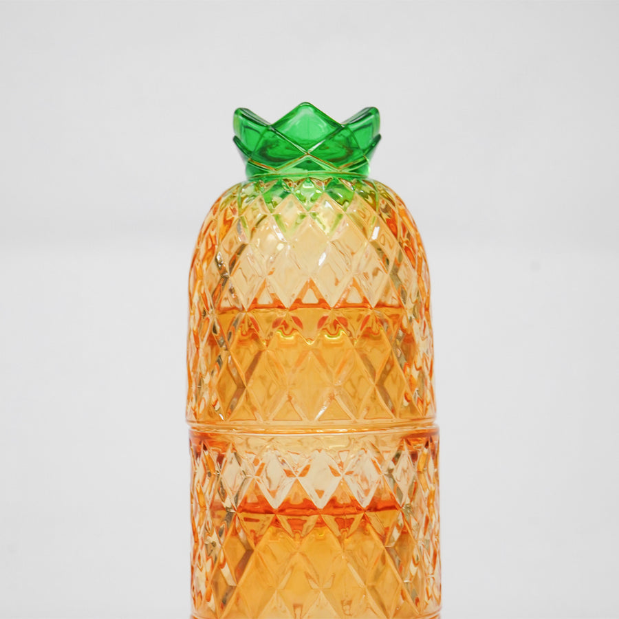 A translucent orange pineapple-shaped container with a textured diamond-cut pattern and a green crown-like top, photographed against a plain light gray background.