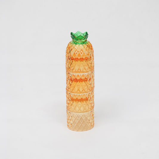 A translucent orange glass container shaped like a pineapple, featuring a textured diamond-patterned body and a green glass crown, set against a plain white background.