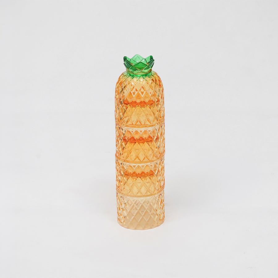 A translucent orange glass container shaped like a pineapple, featuring a textured diamond-patterned body and a green glass crown, set against a plain white background.