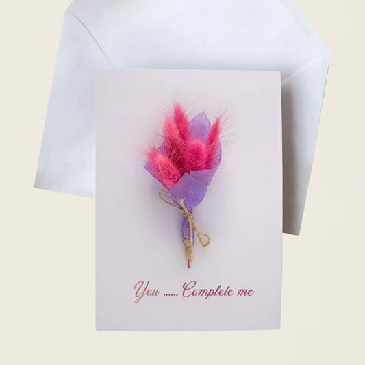 Handmade greeting card featuring a mini magenta pink dried bunny tail bouquet with a white envelope on a light backdrop.