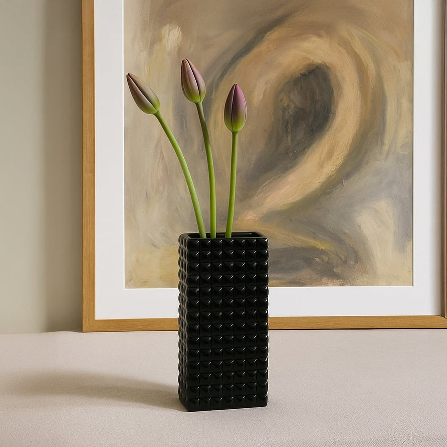 Black textured vase with green floral stems styled near artwork creating bold contrast and modern tabletop Decor accent.