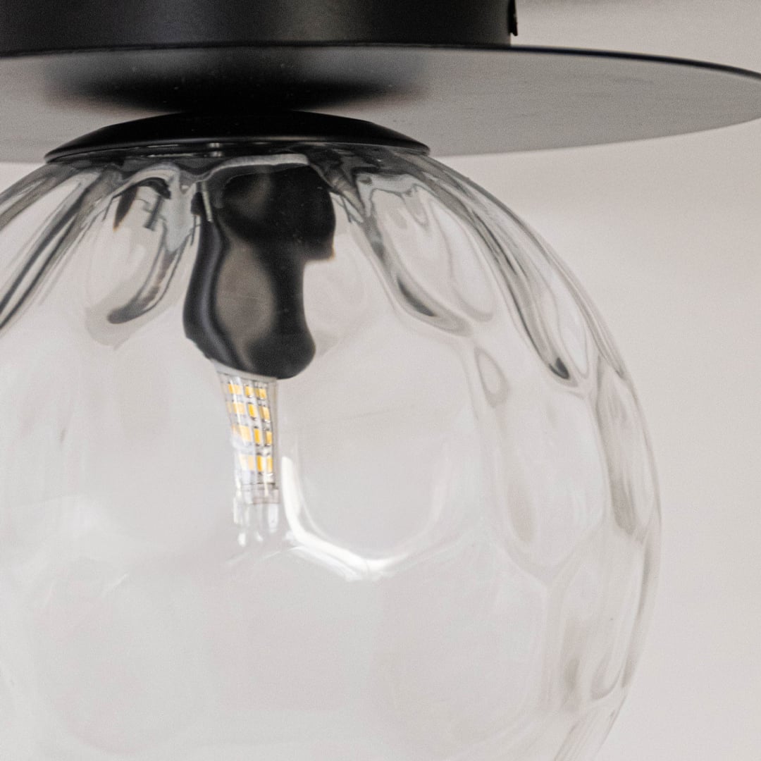 Closeup of ceiling light with clear textured glass globe and black base for elegant modern ceiling lighting and decor.