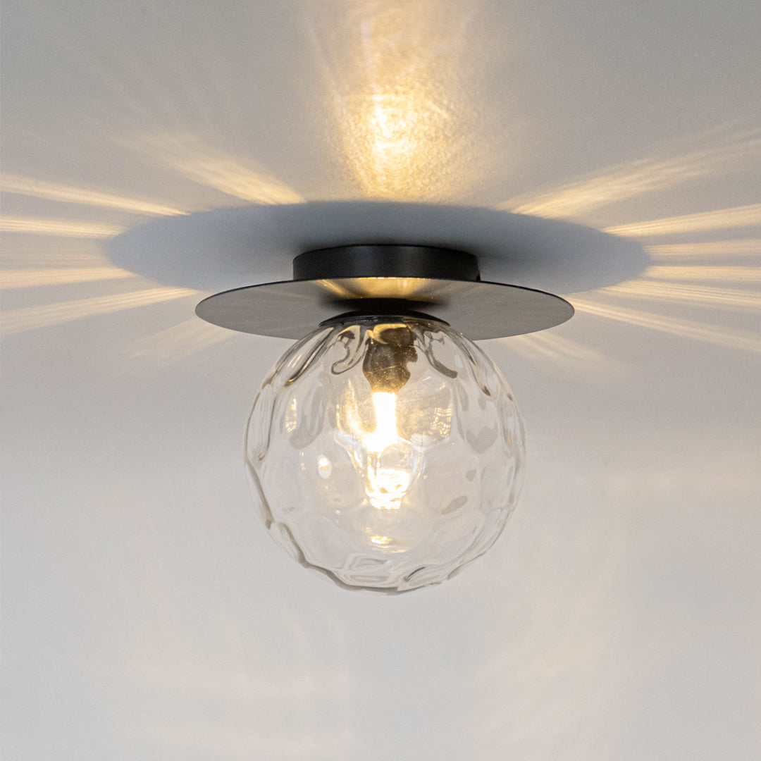 Modern black metal ceiling light with textured glass shade casting decorative light patterns for stylish decor spaces.