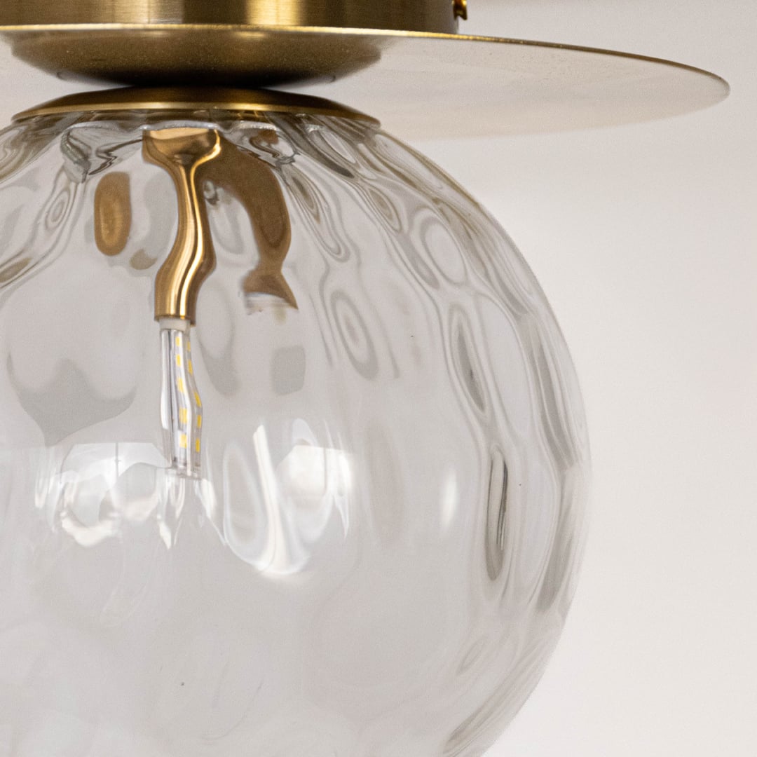 Closeup of gold ceiling light with clear textured glass globe and metal frame for modern ceiling lighting and home decor.