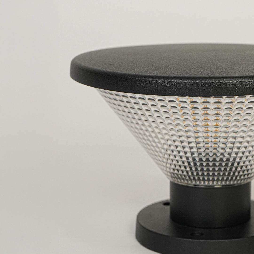 Outdoor pillar light with black metal top and textured glass diffuser mounted on neutral wall background ideal for garden or patio lighting.
