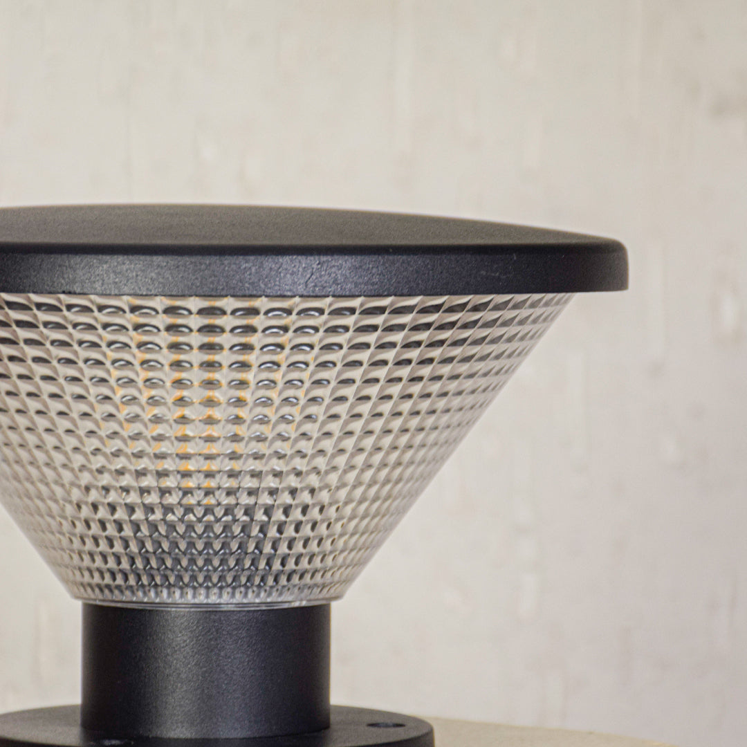 Close view of outdoor pillar light with patterned glass shade and metal base showcasing durable weather resistant exterior lighting design.