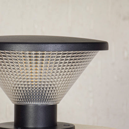Close view of outdoor pillar light with patterned glass shade and metal base showcasing durable weather resistant exterior lighting design.
