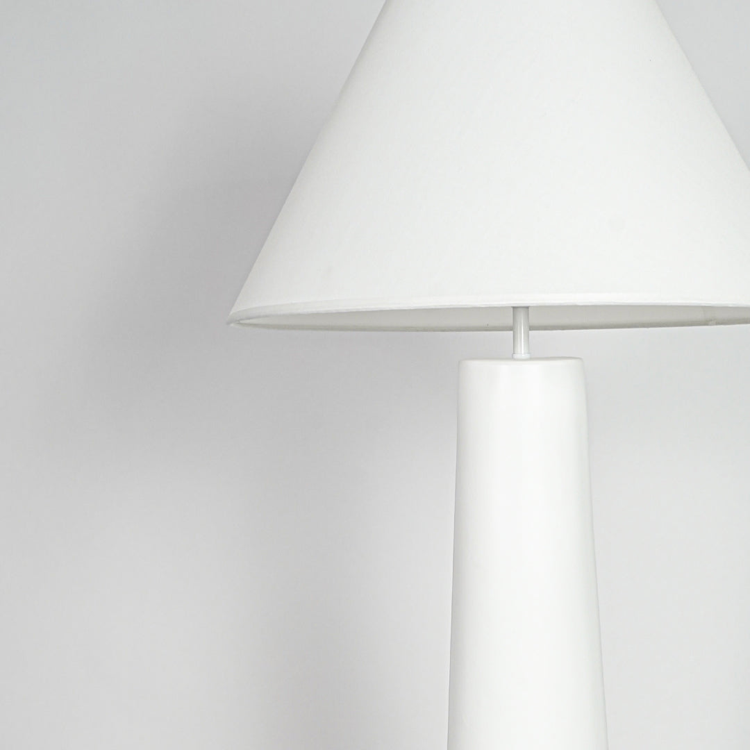 Close view of table lamp with white shade and minimal base design showcasing clean contemporary lighting style on neutral background.